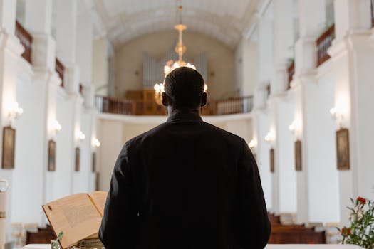 A priest stands before a congregation in a grand church, delivering a sermon with an open Bible.